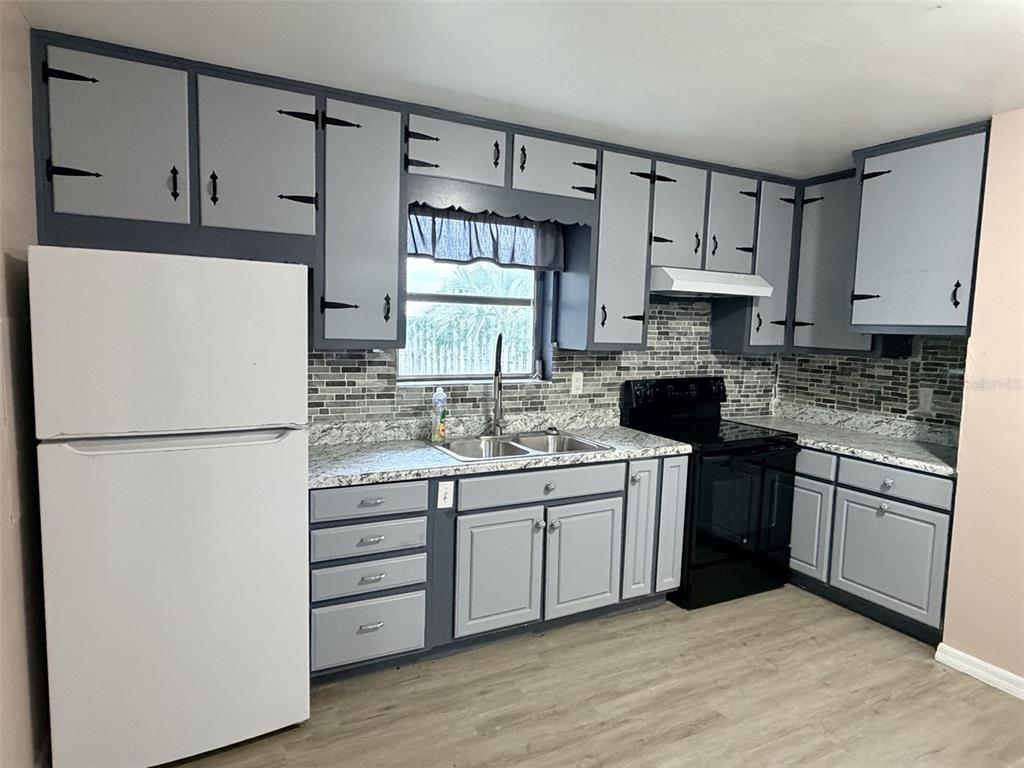 A kitchen features grey cabinets with dark trim, a white refrigerator, and a tiled backsplash — 1025 NE 4TH STREET, CHIEFLAND, FL