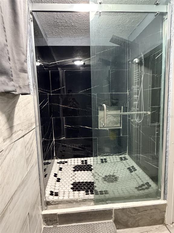 A walk-in shower features black marble-look wall tiles and a black-and-white hexagonal tile floor — 1025 NE 4TH STREET, CHIEFLAND, FL