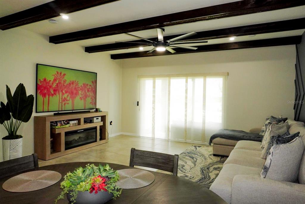 A living room features dark wood ceiling beams, a ceiling fan, and a television console — 1730 DELIGHTFUL DRIVE, DAVENPORT, FL
