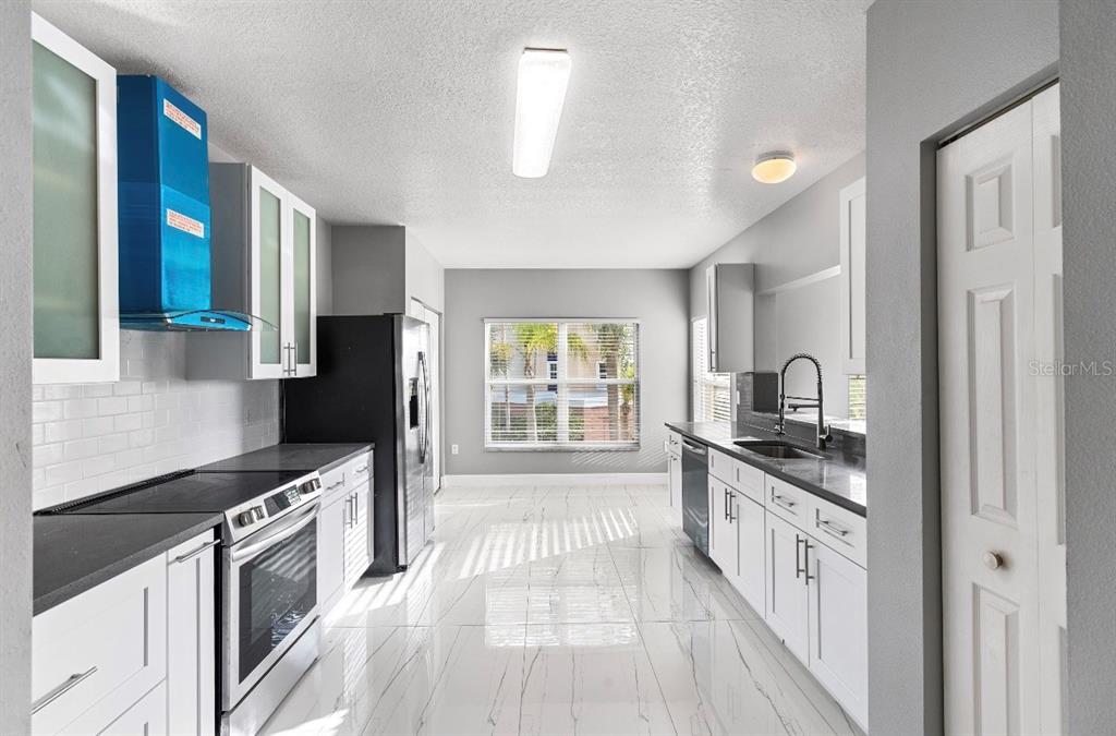 A modern kitchen features white cabinetry, black countertops, stainless steel appliances, and white tiled flooring — 2725 TERRA CEIA BAY BOULEVARD UNIT 201, PALMETTO, FL