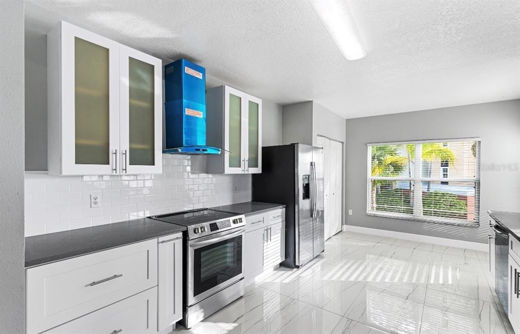 A modern kitchen features white cabinets, stainless steel appliances, a blue range hood, and tile flooring — 2725 TERRA CEIA BAY BOULEVARD UNIT 201, PALMETTO, FL