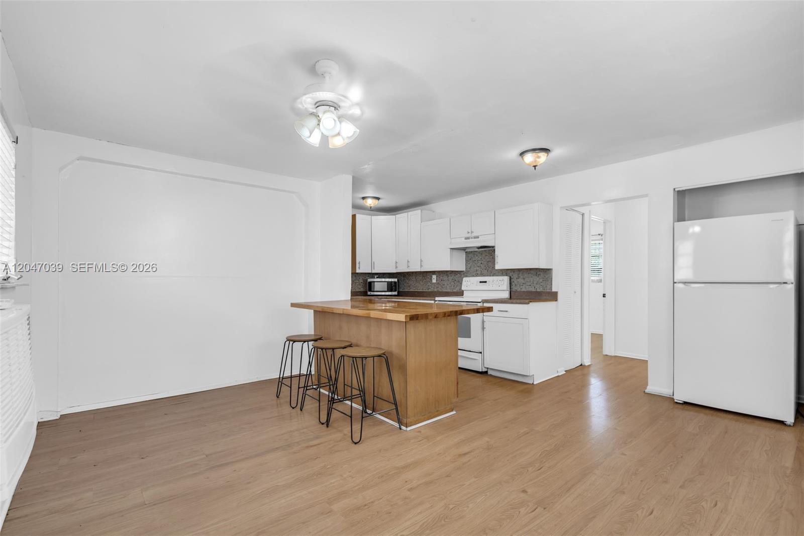 A kitchen features white cabinets, a wooden island with three stools, and light wood flooring — 2809 SW 23rd Ter # 2807, Miami FL 33145, MIAMI, FL