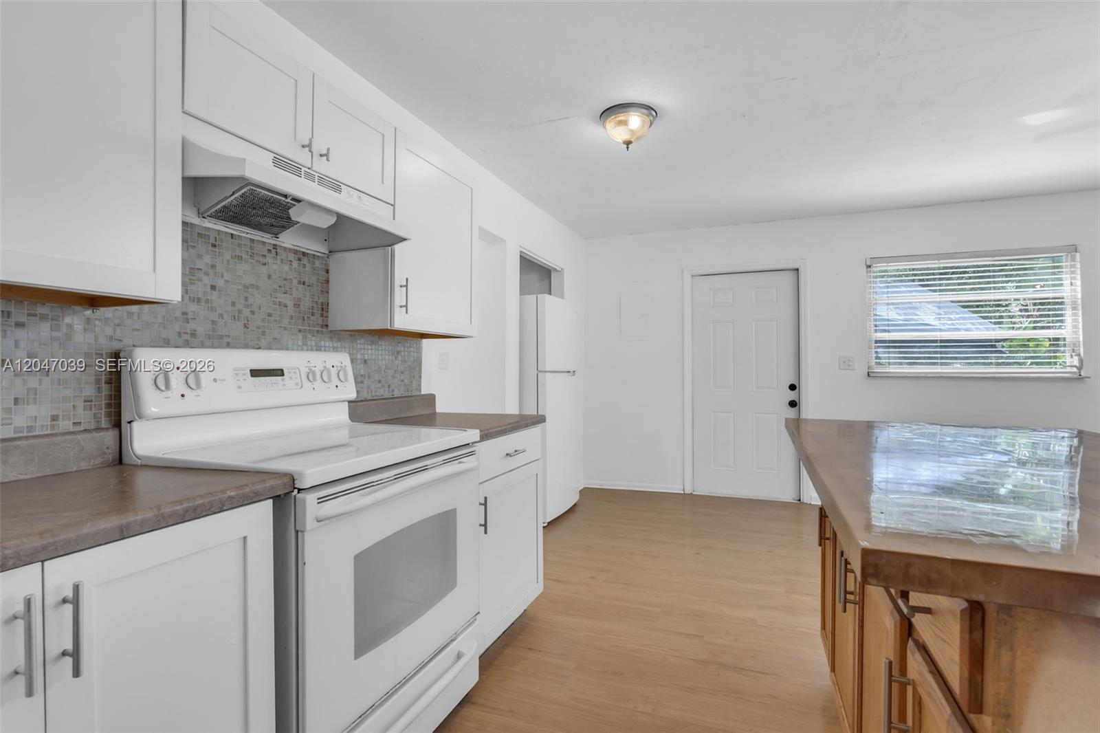 A kitchen features white cabinets, a white stove, a tiled backsplash, and a wooden island — 2809 SW 23rd Ter # 2807, Miami FL 33145, MIAMI, FL