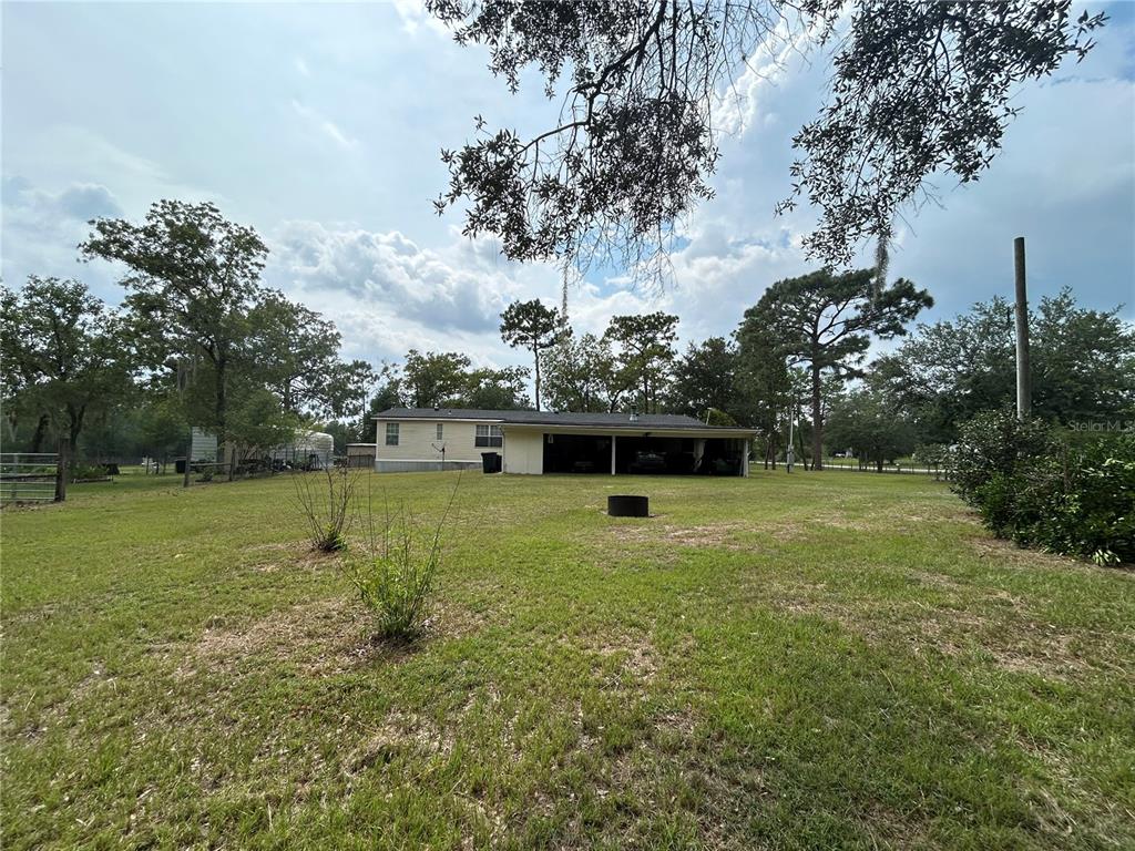 A single-story house with a carport sits on a large, grassy lot with trees — 14050 SE 10TH STREET, WILLISTON, FL