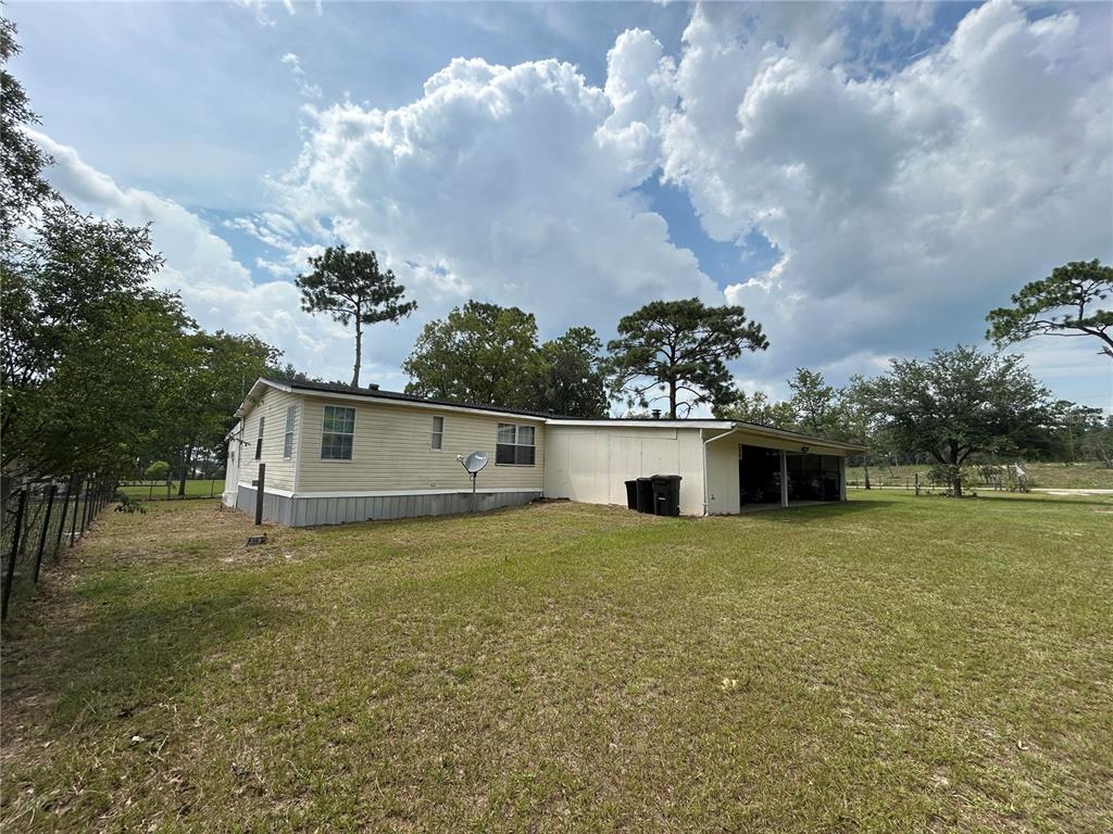 A single-story mobile home with a side carport sits on a large, grassy lot — 14050 SE 10TH STREET, WILLISTON, FL