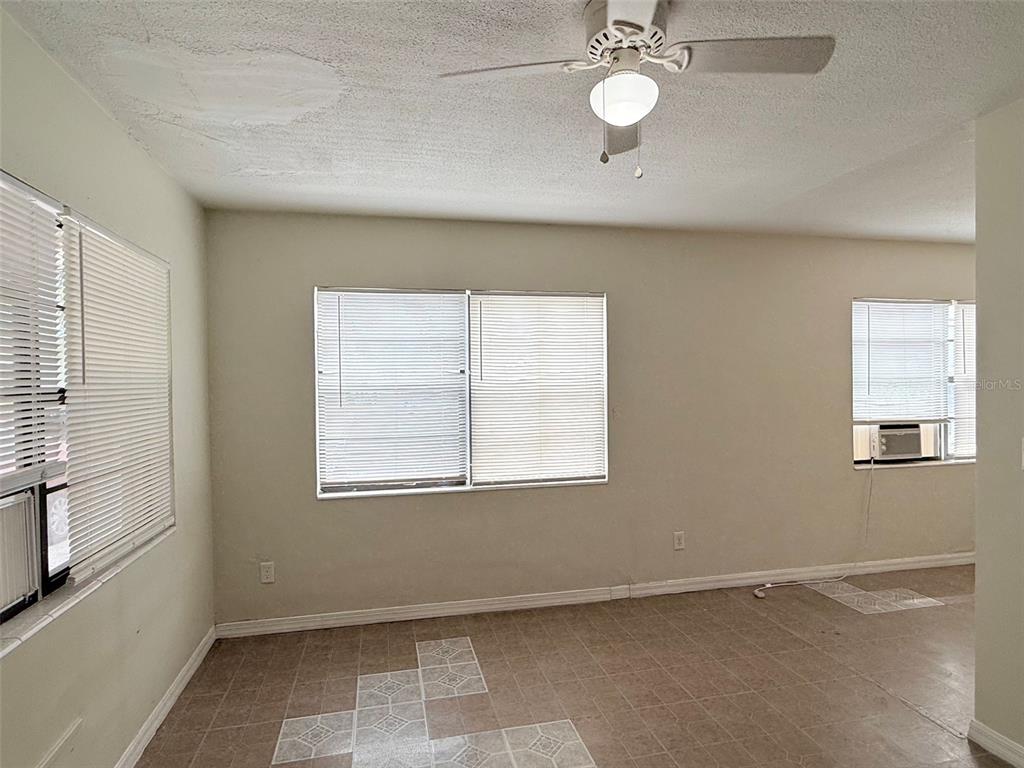 An empty room features light-colored walls, tiled flooring, a ceiling fan, and several windows — 2404 10TH STREET W UNIT 1, BRADENTON, FL