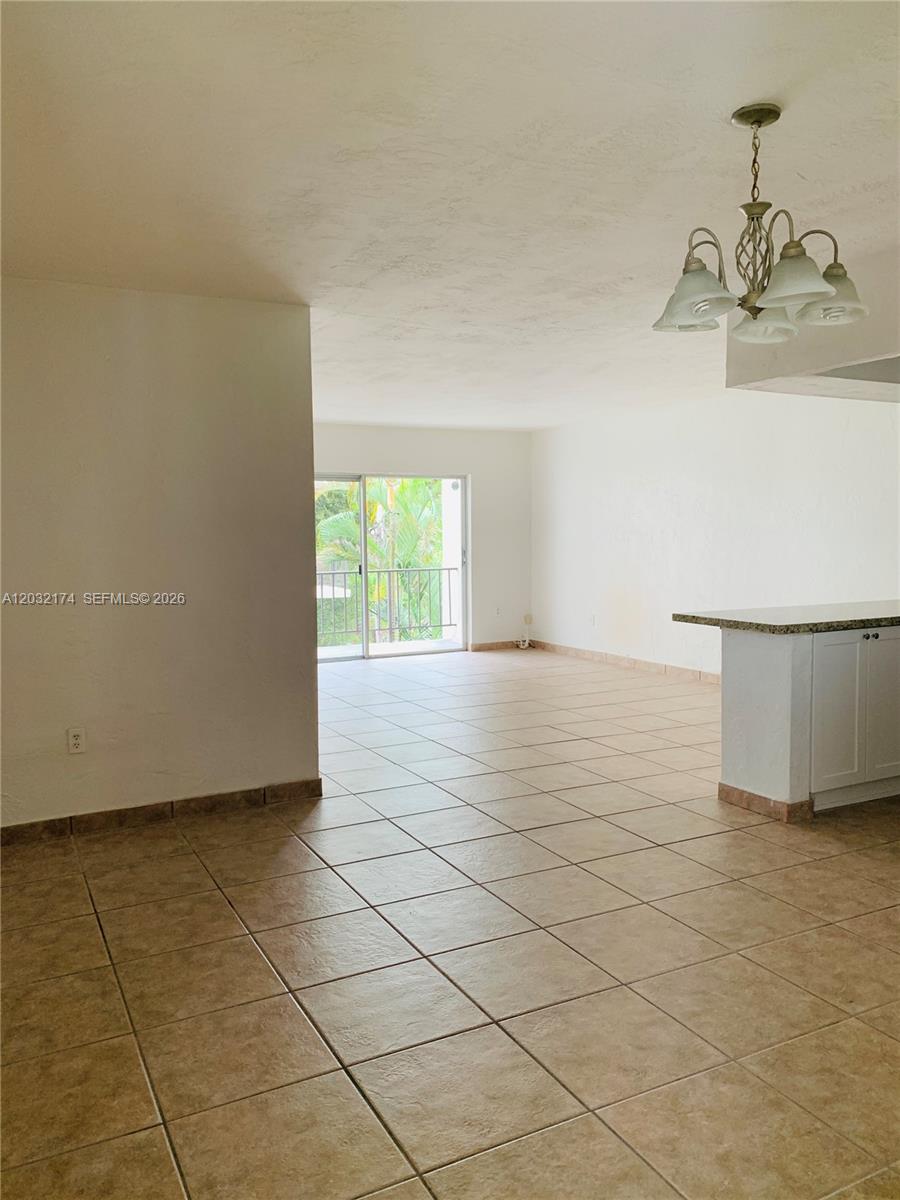An open-concept living area features light-colored tile flooring, white walls, and a sliding glass door — 6900 N Kendall Dr # A304, Pinecrest FL 33156, PINECREST, FL