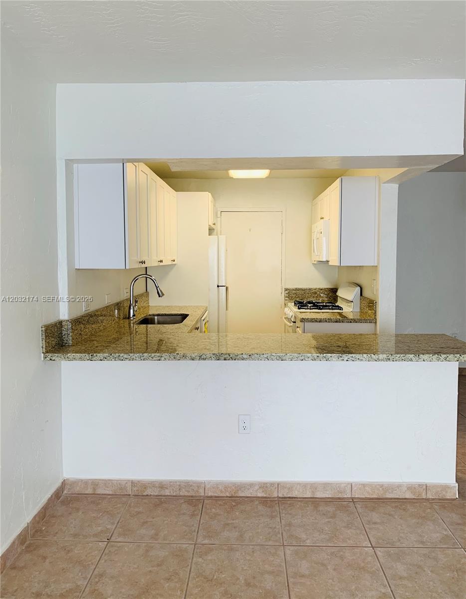 A kitchen features white cabinets, granite countertops, and a breakfast bar overlooking a tiled area — 6900 N Kendall Dr # A304, Pinecrest FL 33156, PINECREST, FL