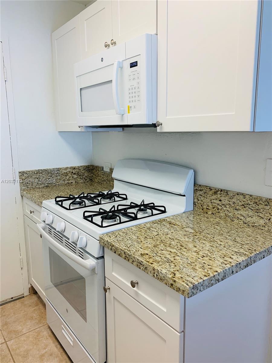 A kitchen features white cabinets, a gas stove, a microwave, and granite countertops — 6900 N Kendall Dr # A304, Pinecrest FL 33156, PINECREST, FL