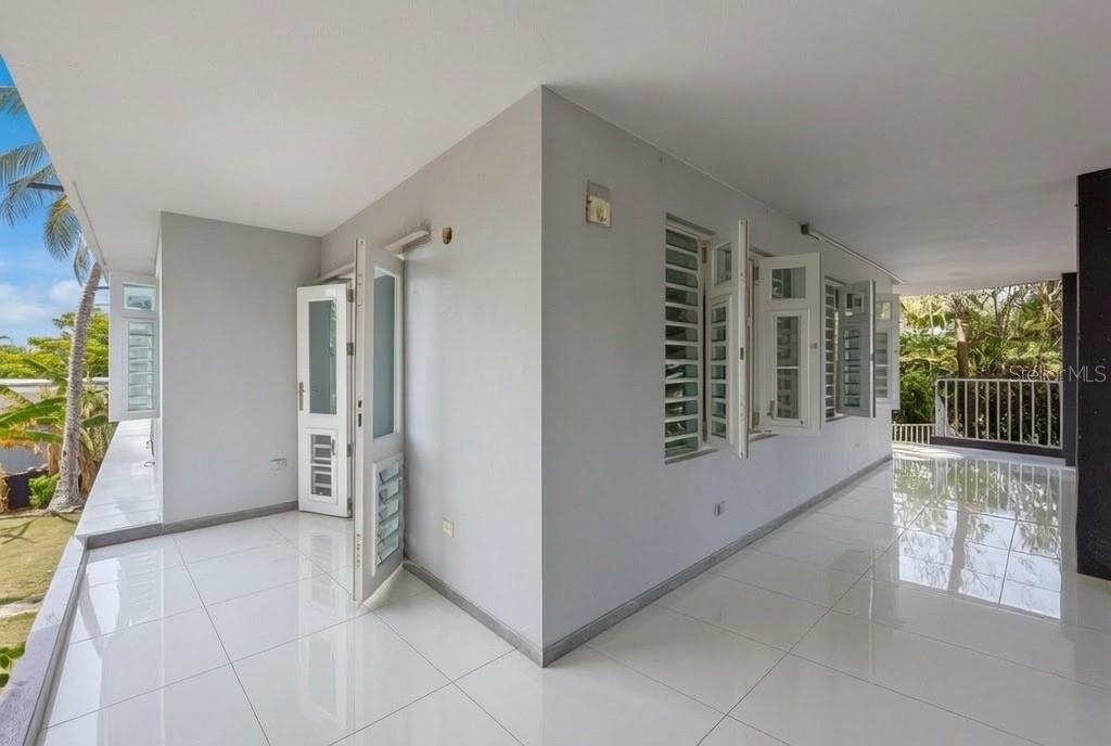 A concrete driveway leads toward a two-story house framed by white metal gates and palm trees — 3-B CALLE KENNEDY, DORADO, PR
