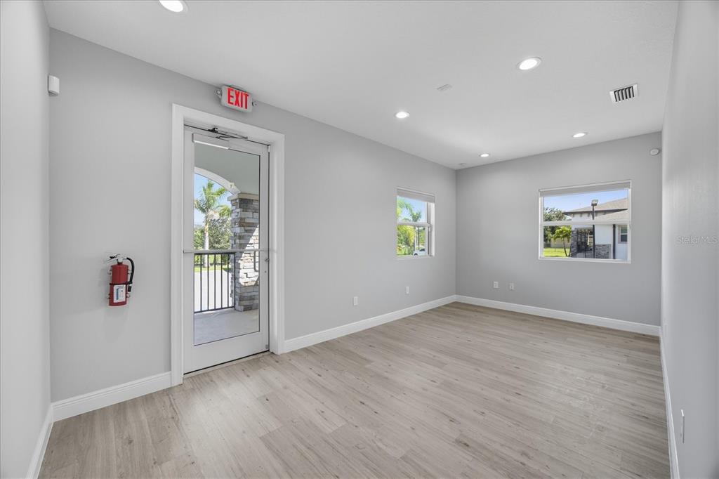 An empty room with light gray walls, wood-look flooring, recessed lighting, and an exit door — 10305 US HIGHWAY 41 N, PALMETTO, FL