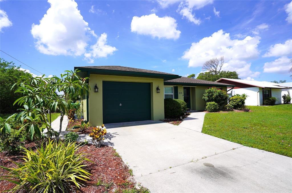 A single-story house with a green garage door, a concrete driveway, and a landscaped yard — 515 MERIDAN AVENUE NW, PORT CHARLOTTE, FL