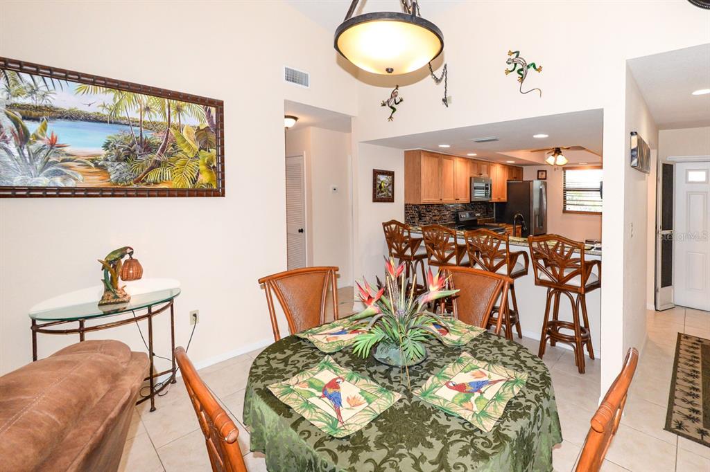 A dining area with a round table and chairs opens to a kitchen with bar seating — 335 COLDEWAY DRIVE UNIT F21, PUNTA GORDA, FL