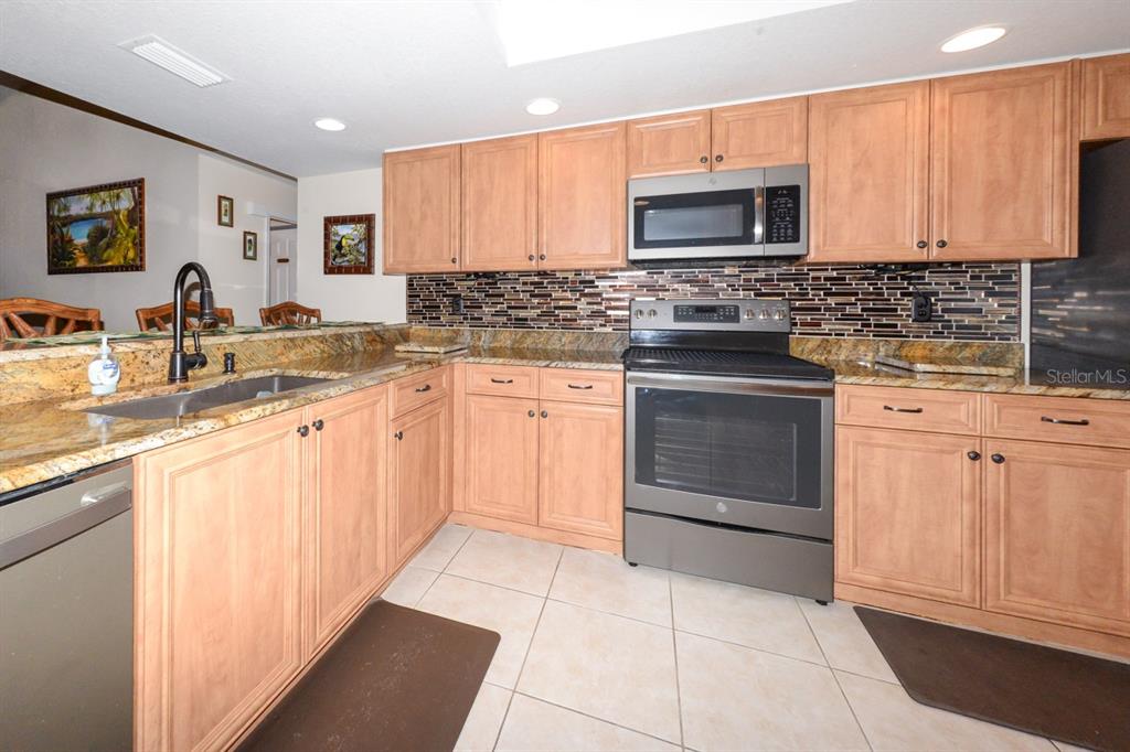A kitchen features light wood cabinets, granite countertops, stainless steel appliances, and a tiled backsplash — 335 COLDEWAY DRIVE UNIT F21, PUNTA GORDA, FL
