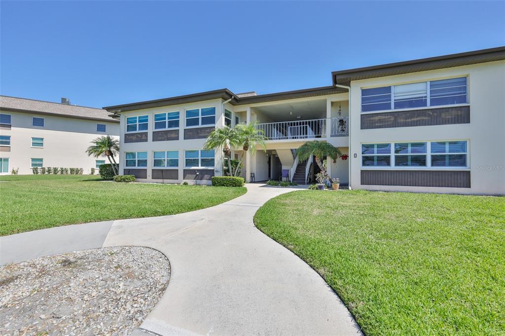 A concrete walkway leads to the entrance of a two-story apartment building with lawn — 4736 JASPER DR UNIT 103, NEW PORT RICHEY, FL