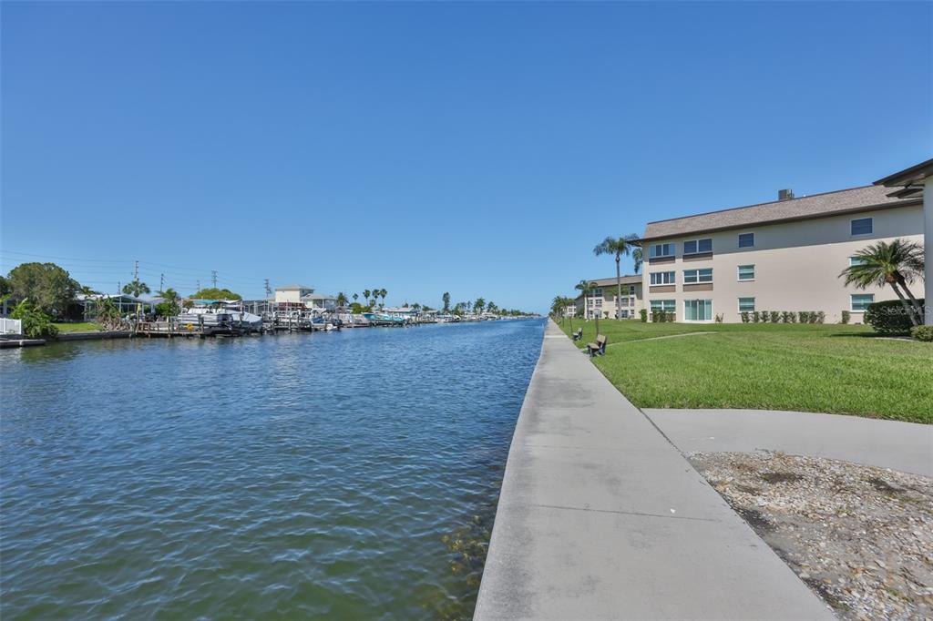 A concrete walkway runs alongside a canal lined with docked boats and apartment buildings — 4736 JASPER DR UNIT 103, NEW PORT RICHEY, FL