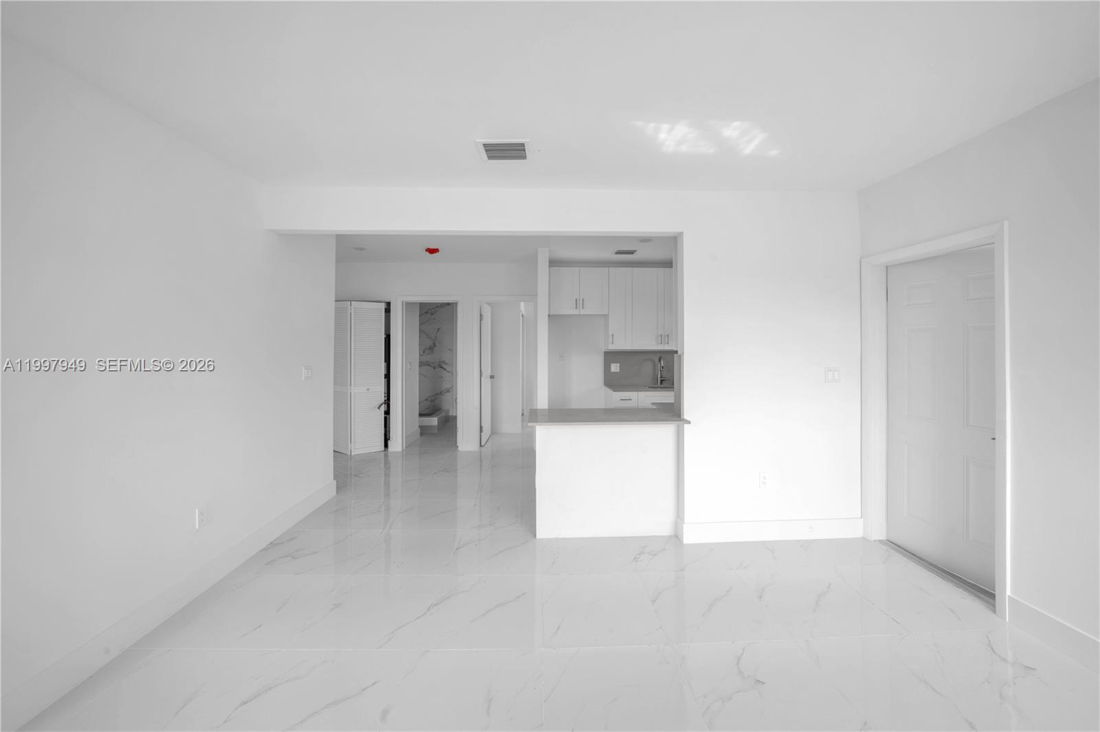 A bright, minimalist room features white walls, white marble-look tile flooring, and a small kitchen — 450 Beacom Blvd, Miami FL 33135, MIAMI, FL