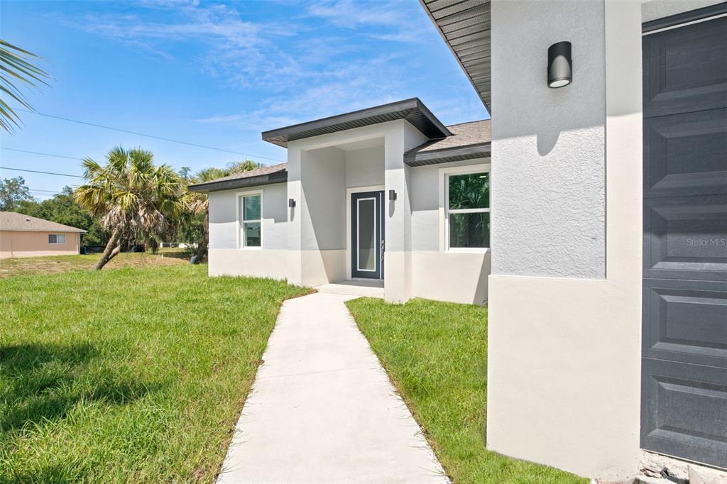 A concrete walkway leads to the front entrance of a modern, light-colored stucco home — 2830 BILLBERRY STREET, NORTH PORT, FL
