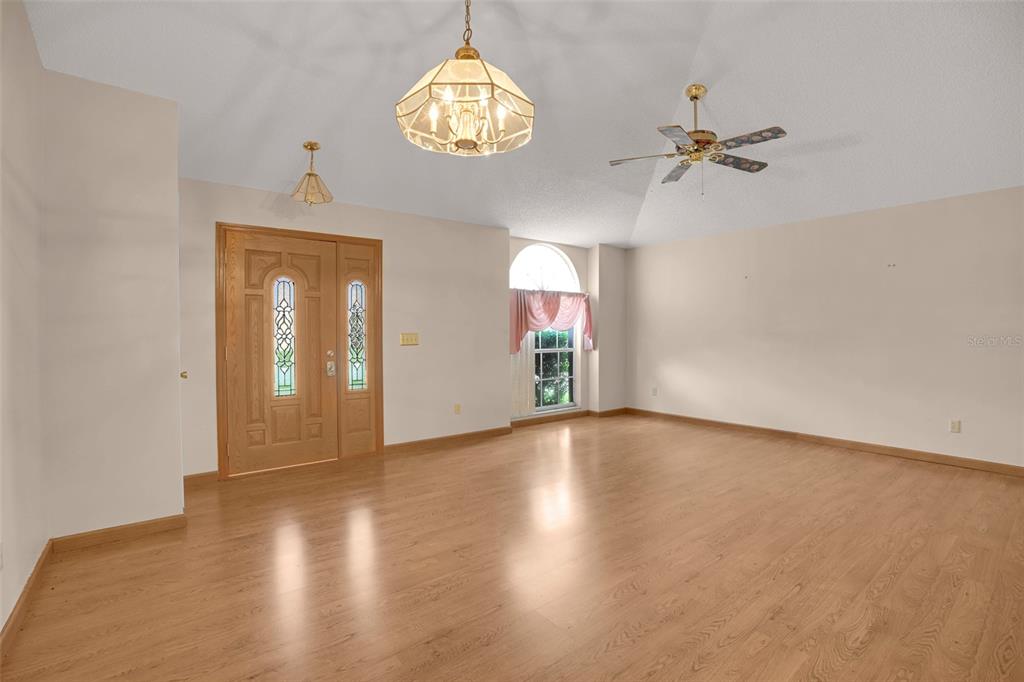 An empty room with light wood flooring, a vaulted ceiling, and a wooden front door — 9554 BRACKIN STREET, ORLANDO, FL