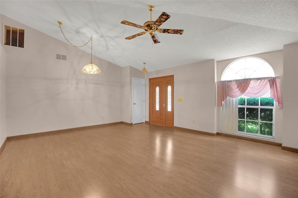 An empty room features light wood flooring, a vaulted ceiling, and a wooden front door — 9554 BRACKIN STREET, ORLANDO, FL