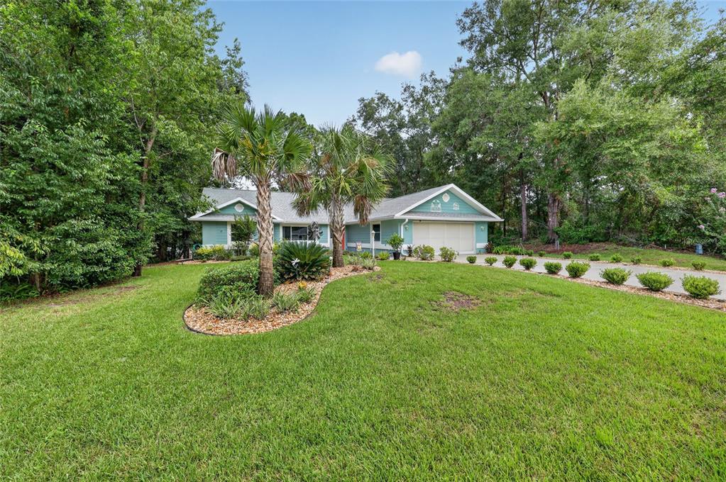 A teal, single-story house with a two-car garage sits behind a landscaped lawn and trees — 19683 SW 93RD LANE, DUNNELLON, FL