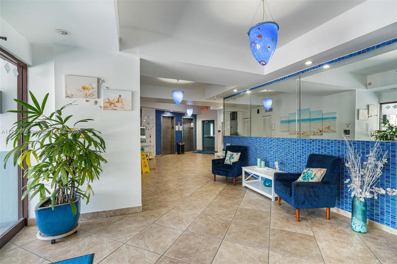 A bright lobby features tiled floors, blue accent walls, two armchairs, and elevator access — 7300 Wayne Ave # 317, Miami Beach FL 33141, MIAMI BEACH, FL