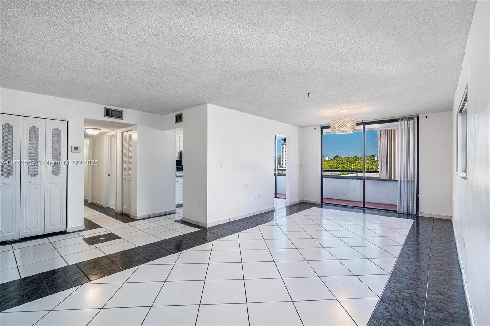 An empty living room features white and black tiled floors, white walls, and a balcony — 7300 Wayne Ave # 317, Miami Beach FL 33141, MIAMI BEACH, FL