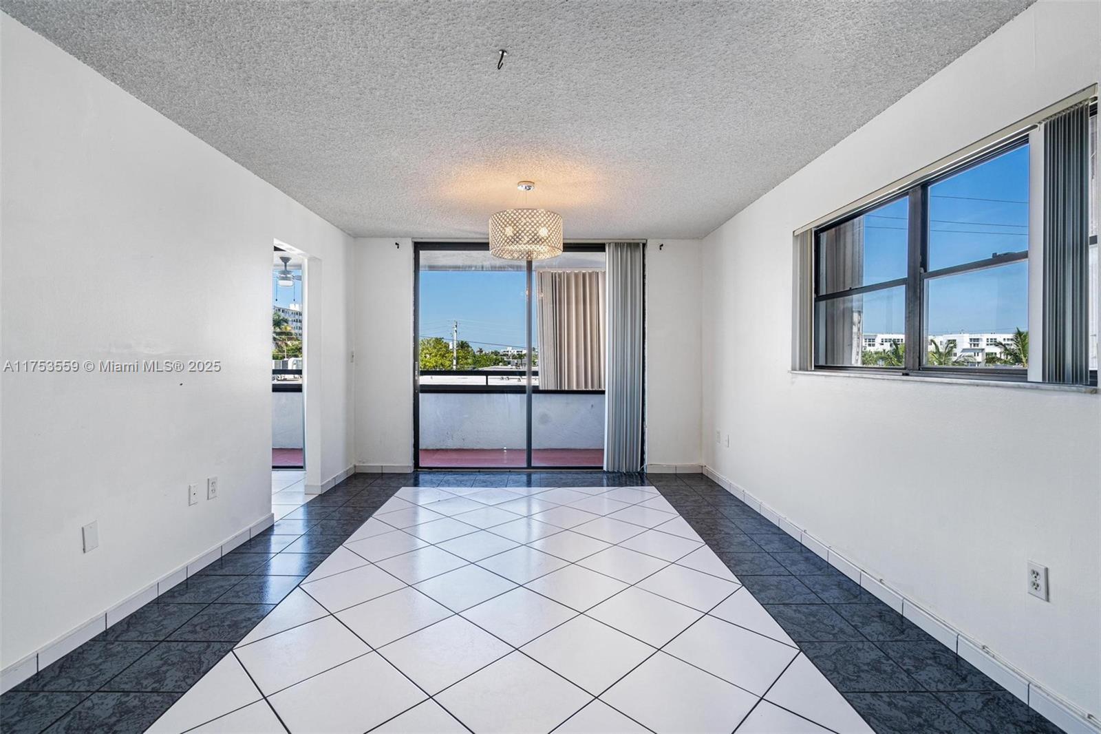 A dining area features white and dark tile flooring, a central chandelier, and a sliding glass door — 7300 Wayne Ave # 317, Miami Beach FL 33141, MIAMI BEACH, FL