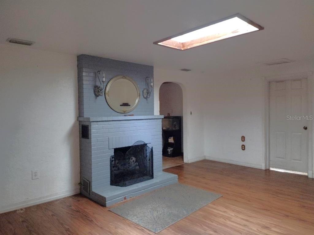 A living room features a gray painted brick fireplace, wood-look flooring, and a rectangular skylight — 651 OLD HAW CREEK ROAD, BUNNELL, FL