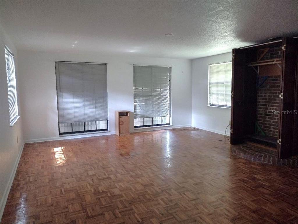 An empty room features parquet wood flooring, white walls, multiple windows, and a brick fireplace — 651 OLD HAW CREEK ROAD, BUNNELL, FL