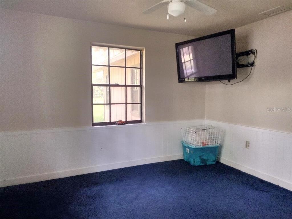 A room with blue carpet, white wainscoting, a window, and a wall-mounted television — 651 OLD HAW CREEK ROAD, BUNNELL, FL