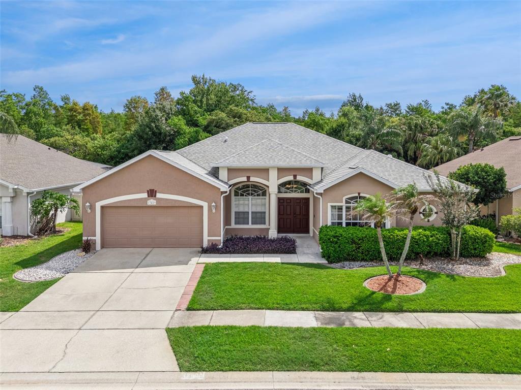 A single-story tan stucco house with a two-car garage and a landscaped front yard — 13429 FALCON POINTE DRIVE, ORLANDO, FL