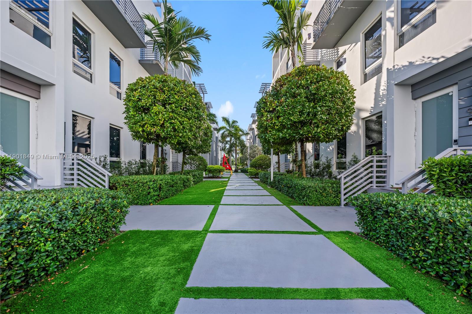 A paved walkway lined with manicured hedges and trees leads between two modern residential buildings — 9153 NW 33rd St, Doral FL 33172, DORAL, FL