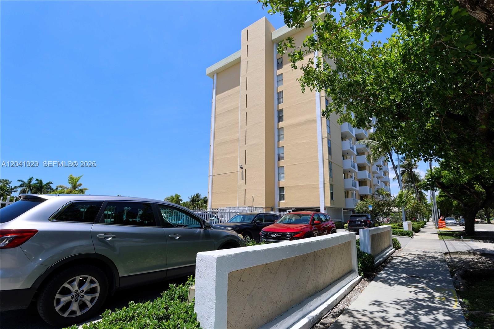 A multi-story beige apartment building stands behind a parking lot and a sidewalk — 2000 NE 135th St # 906, North Miami FL 33181, NORTH MIAMI, FL