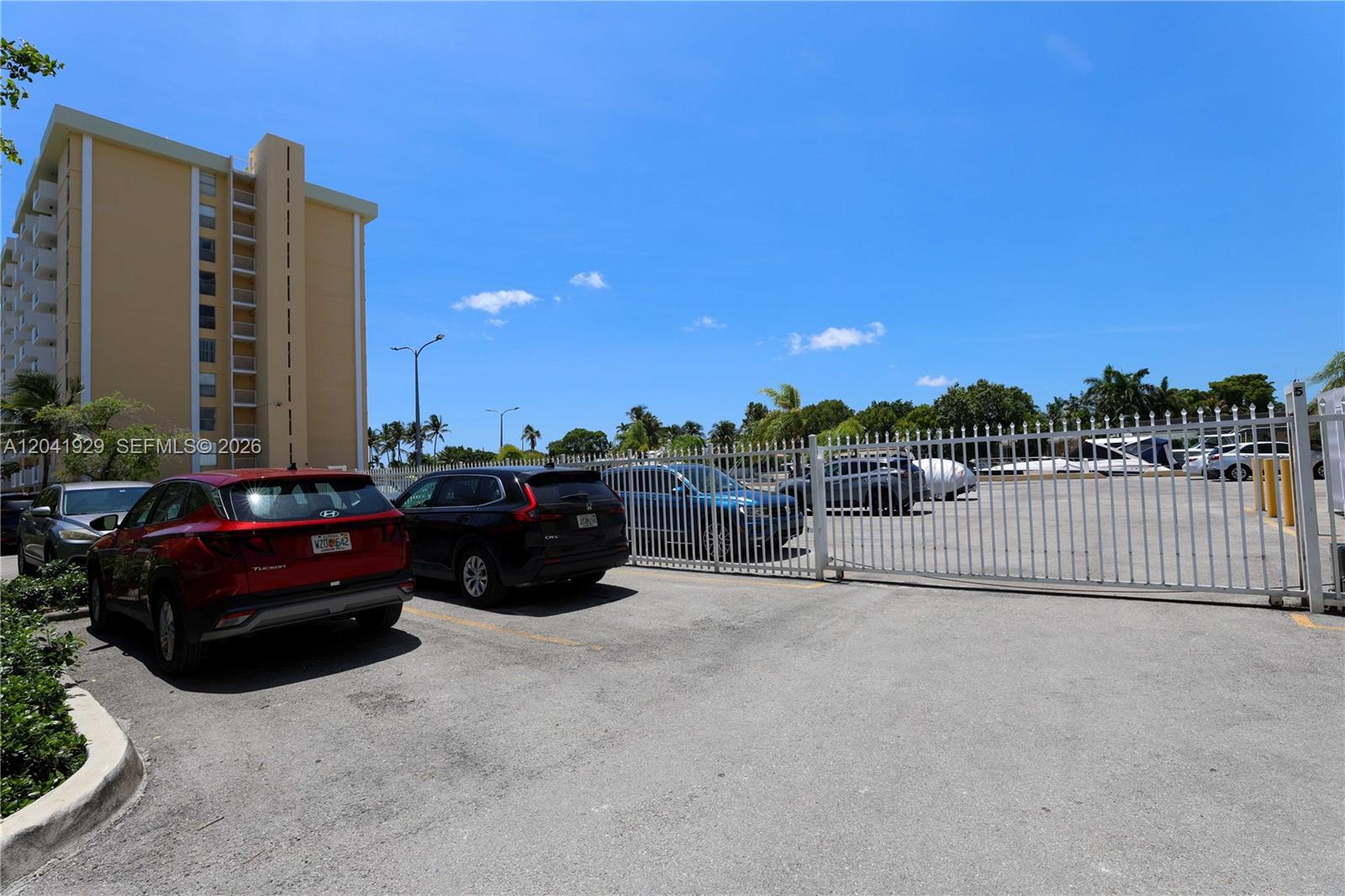 A parking lot with several cars sits next to a tall apartment building — 2000 NE 135th St # 906, North Miami FL 33181, NORTH MIAMI, FL