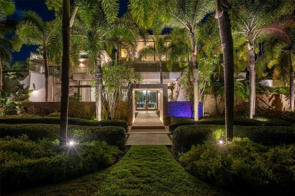 A modern house exterior at night features a stone walkway, manicured hedges, and palm trees — 200 DORADO BEACH DRIVE UNIT 2210, DORADO, PR