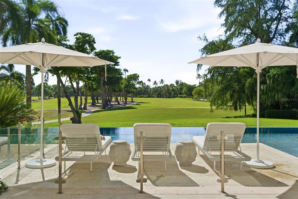 A patio with three lounge chairs and umbrellas overlooks an infinity pool and golf course — 200 DORADO BEACH DRIVE UNIT 2210, DORADO, PR