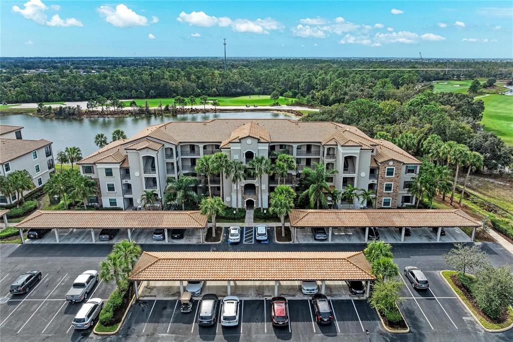 An apartment building exterior features a covered parking structure in front of the main entrance — 16706 VARDON TERRACE UNIT 208, LAKEWOOD RANCH, FL
