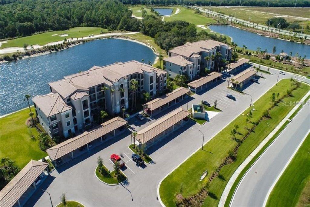 An aerial view shows two multi-story apartment buildings with covered parking lots near a lake — 16706 VARDON TERRACE UNIT 208, LAKEWOOD RANCH, FL