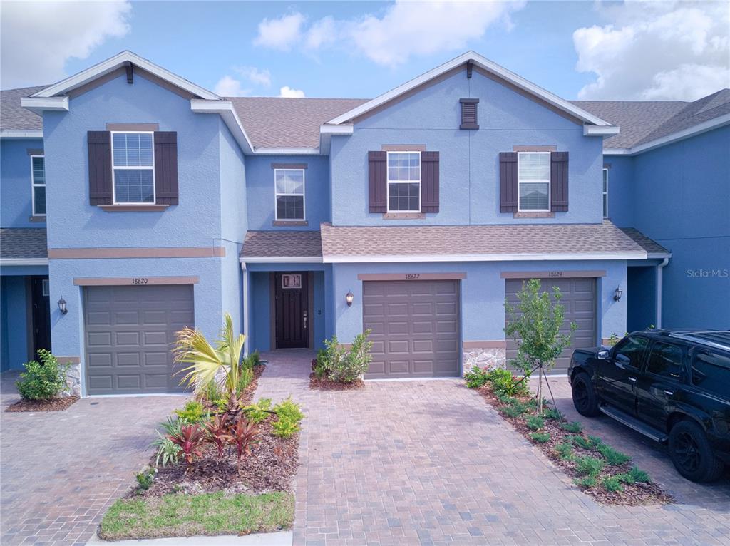 A blue multi-unit townhouse exterior features three garage doors and a paved driveway — 18622 NOBLE CASPIAN DRIVE, LUTZ, FL