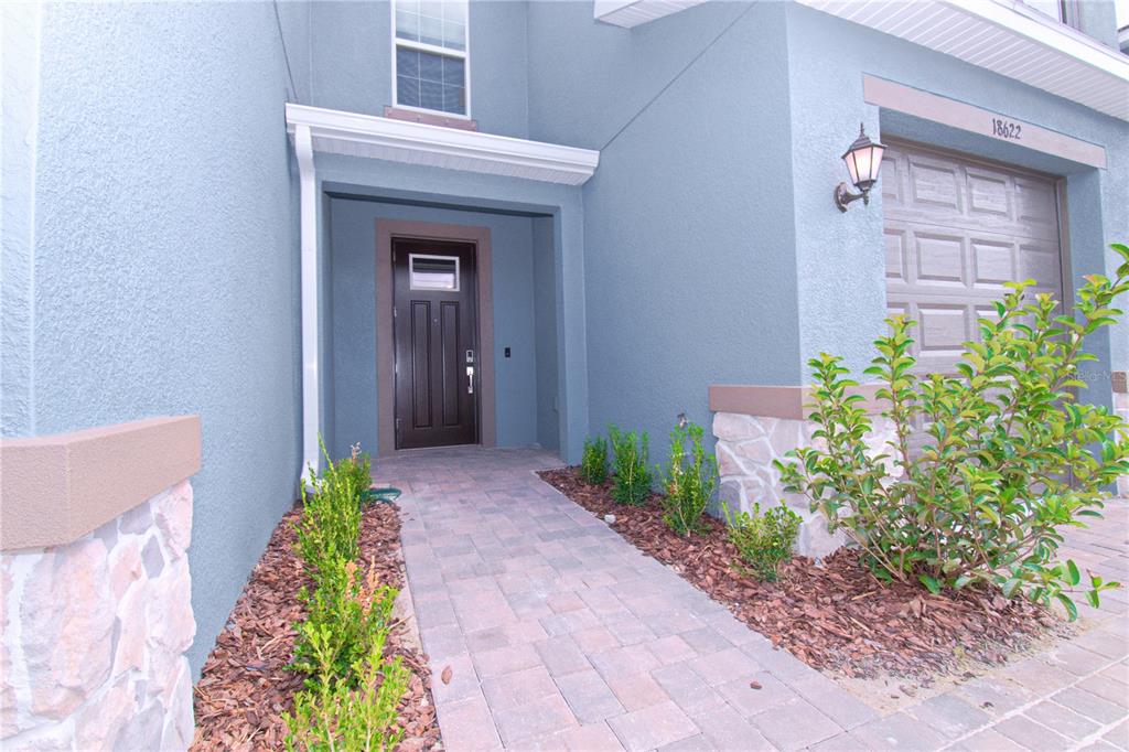 A paved walkway leads to the front door of a blue house with stone accents — 18622 NOBLE CASPIAN DRIVE, LUTZ, FL