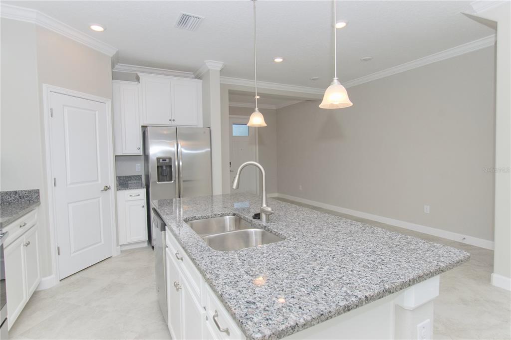 A kitchen features white cabinets, granite countertops, a central island with a sink, and pendant lighting — 18622 NOBLE CASPIAN DRIVE, LUTZ, FL