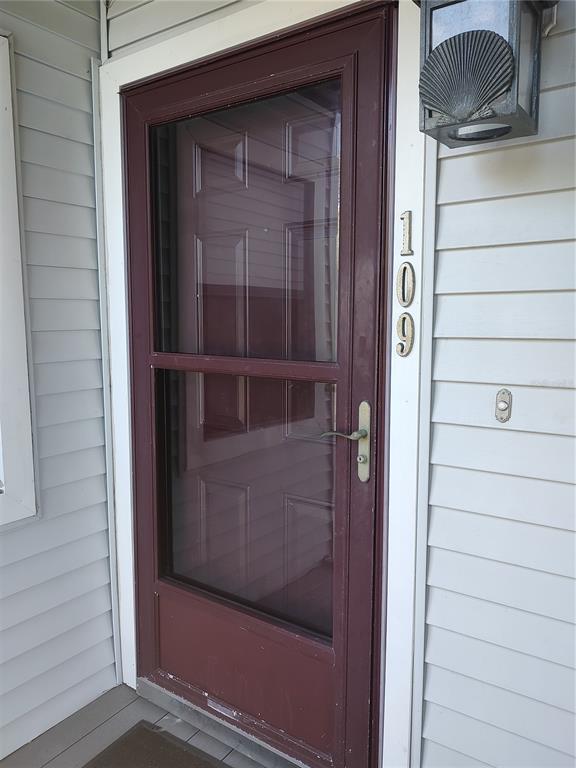 A maroon storm door with a glass panel is mounted on a light-colored vinyl-sided exterior — 515 LEFFINGWELL AVENUE UNIT 109, ELLENTON, FL