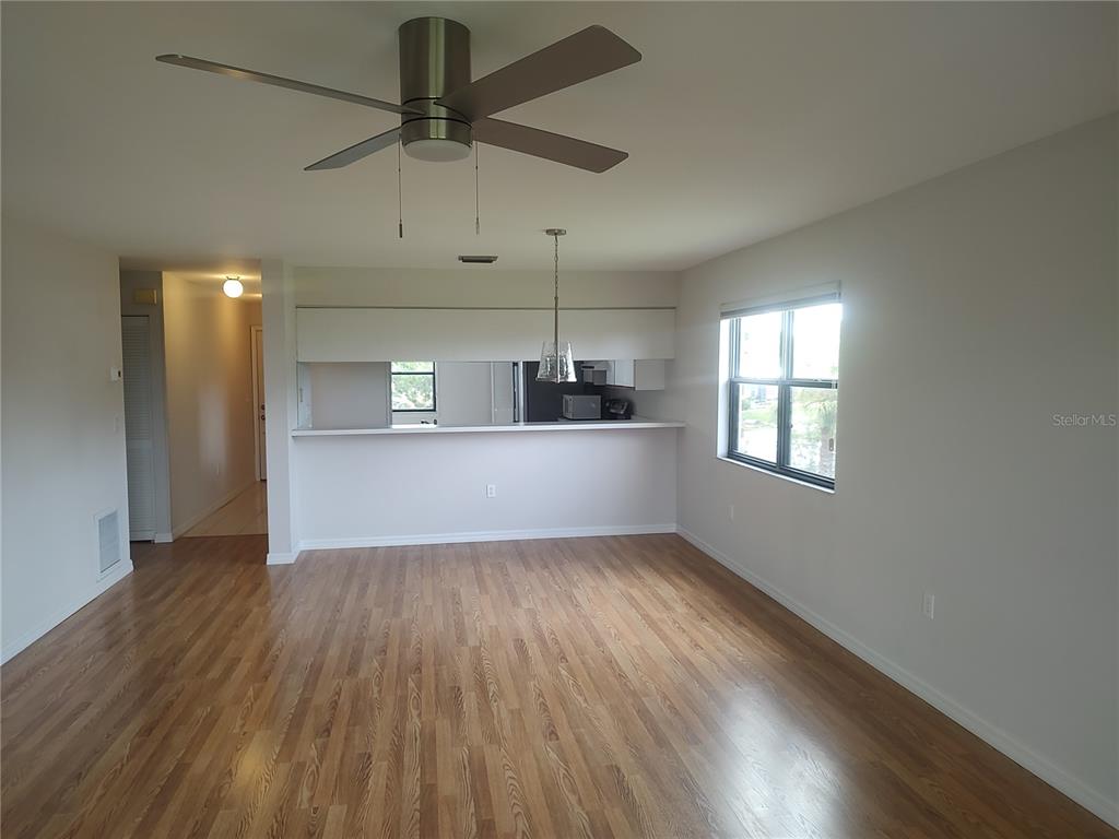 An open living area features wood-look flooring, a ceiling fan, and a kitchen pass-through window — 515 LEFFINGWELL AVENUE UNIT 109, ELLENTON, FL