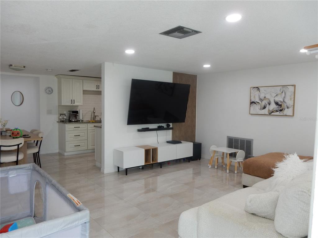 An open-concept living room features a wall-mounted television, white cabinetry, and light-colored tile flooring — 7124 ASHWOOD DRIVE, PORT RICHEY, FL