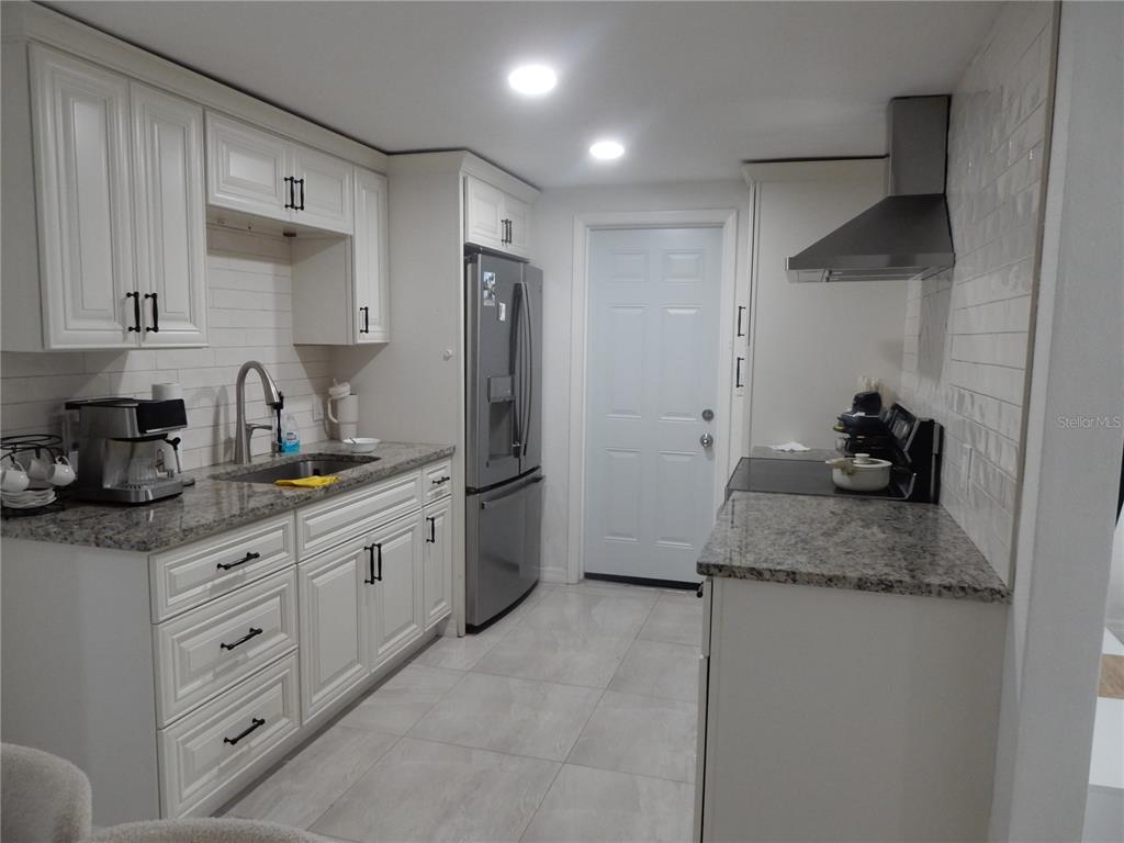 A kitchen features white cabinets, granite countertops, stainless steel appliances, and light-colored tile flooring — 7124 ASHWOOD DRIVE, PORT RICHEY, FL