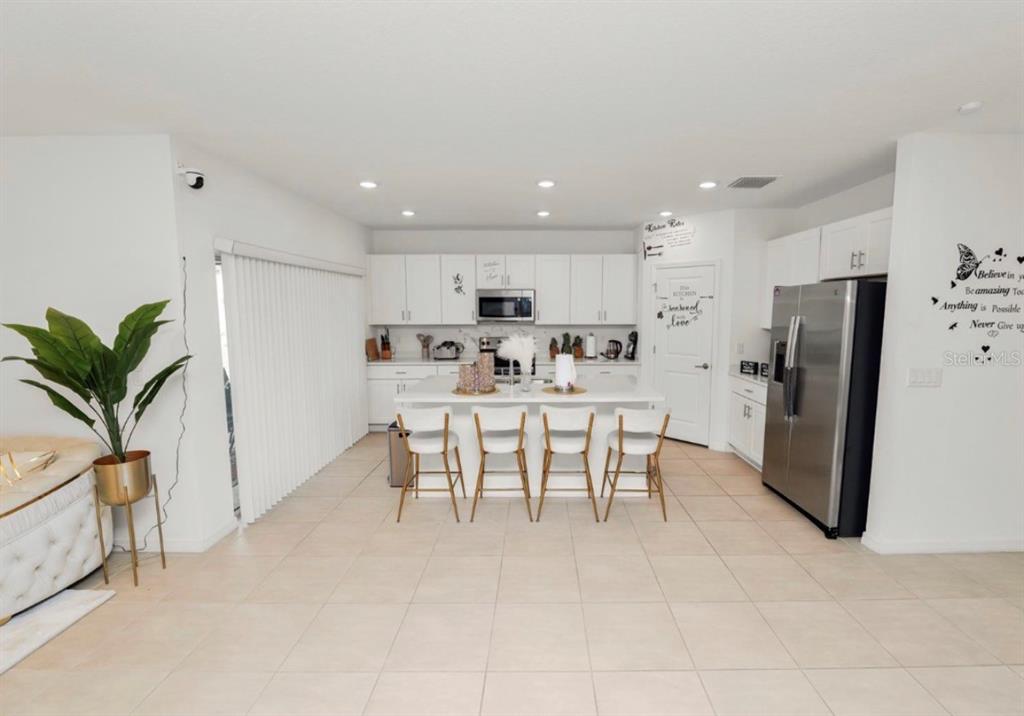 A bright kitchen features white cabinetry, a central island with four stools, and tile flooring — 2039 ROSEWOOD CIRCLE, LAKELAND, FL