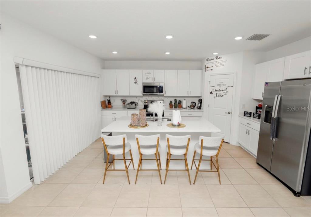 A modern white kitchen features a central island with four chairs and stainless steel appliances — 2039 ROSEWOOD CIRCLE, LAKELAND, FL