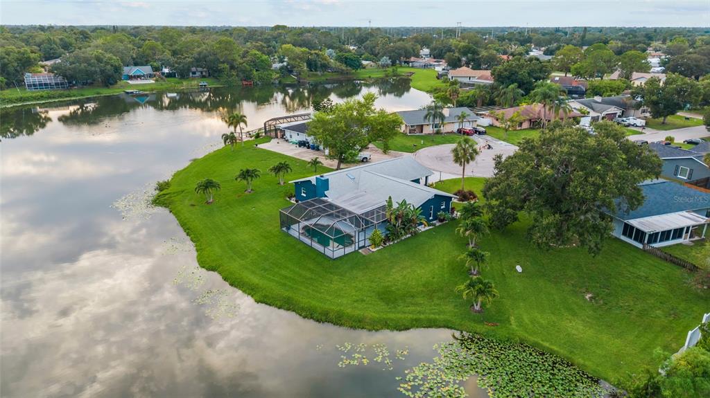 An aerial view shows a blue house with a screened pool on a lakefront lot — 1401 GEORGETOWNE DRIVE, SARASOTA, FL