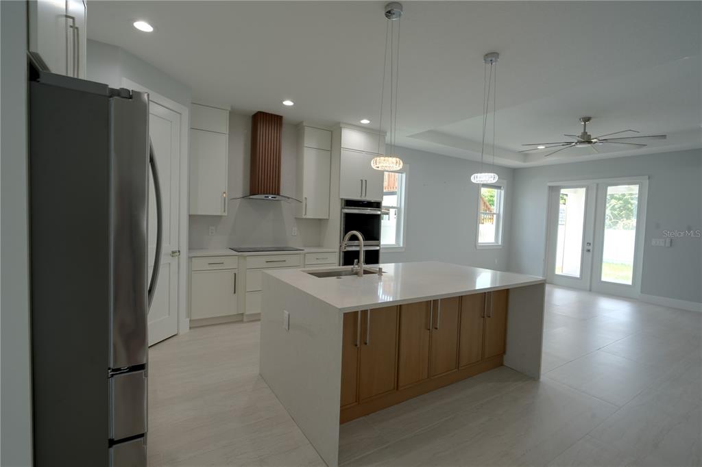A modern kitchen features white cabinets, a wood-accented range hood, and a central quartz island — 7006 THATCHER AVE UNIT A, TAMPA, FL